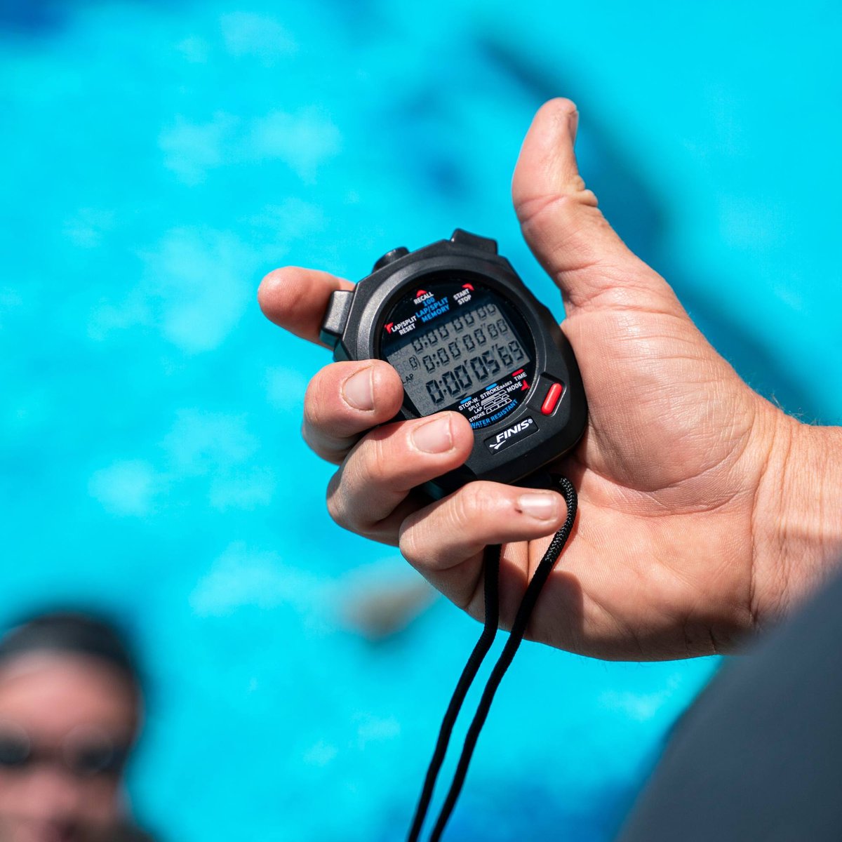 Cronometru FINIS 3X100M negru, ținut în mână deasupra bazinului